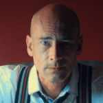 chief dupont, a bald man in a white dress shirt and striped suspenders